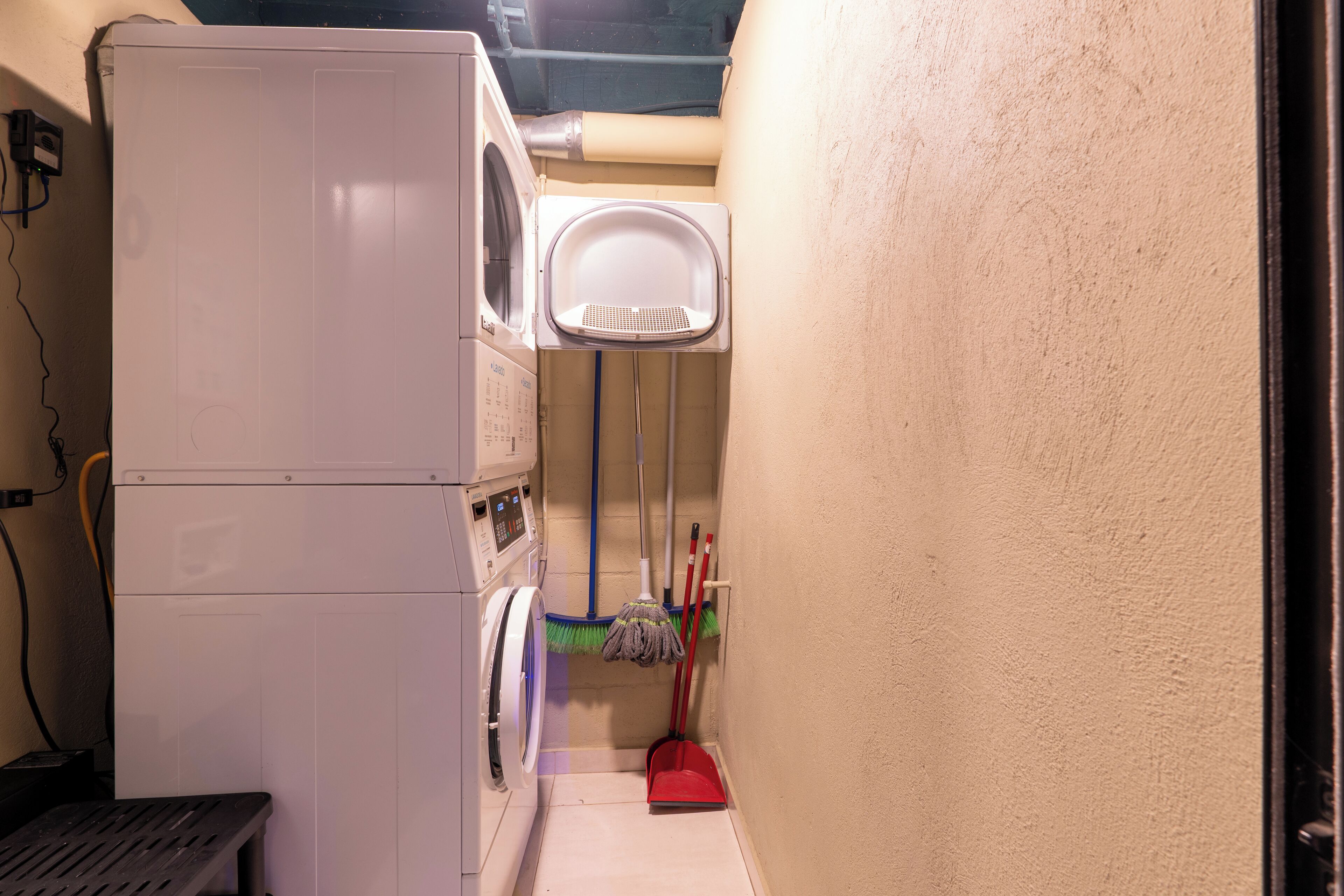 A laundry room with a washing machine, a drying rack, and a broom.