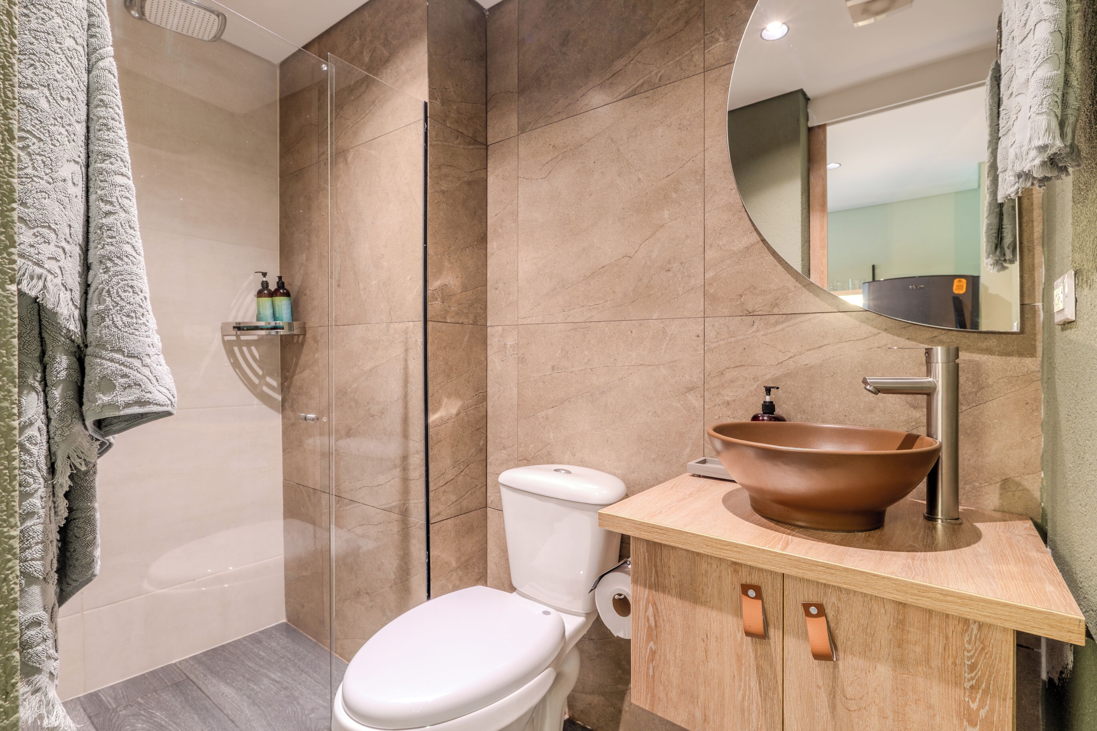 A modern bathroom with a white toilet, a wooden vanity with a large vessel sink, and a glass-enclosed shower.