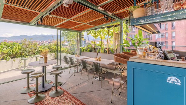 Una terraza en la azotea con mesas y sillas, una zona de bar y vistas a la ciudad.