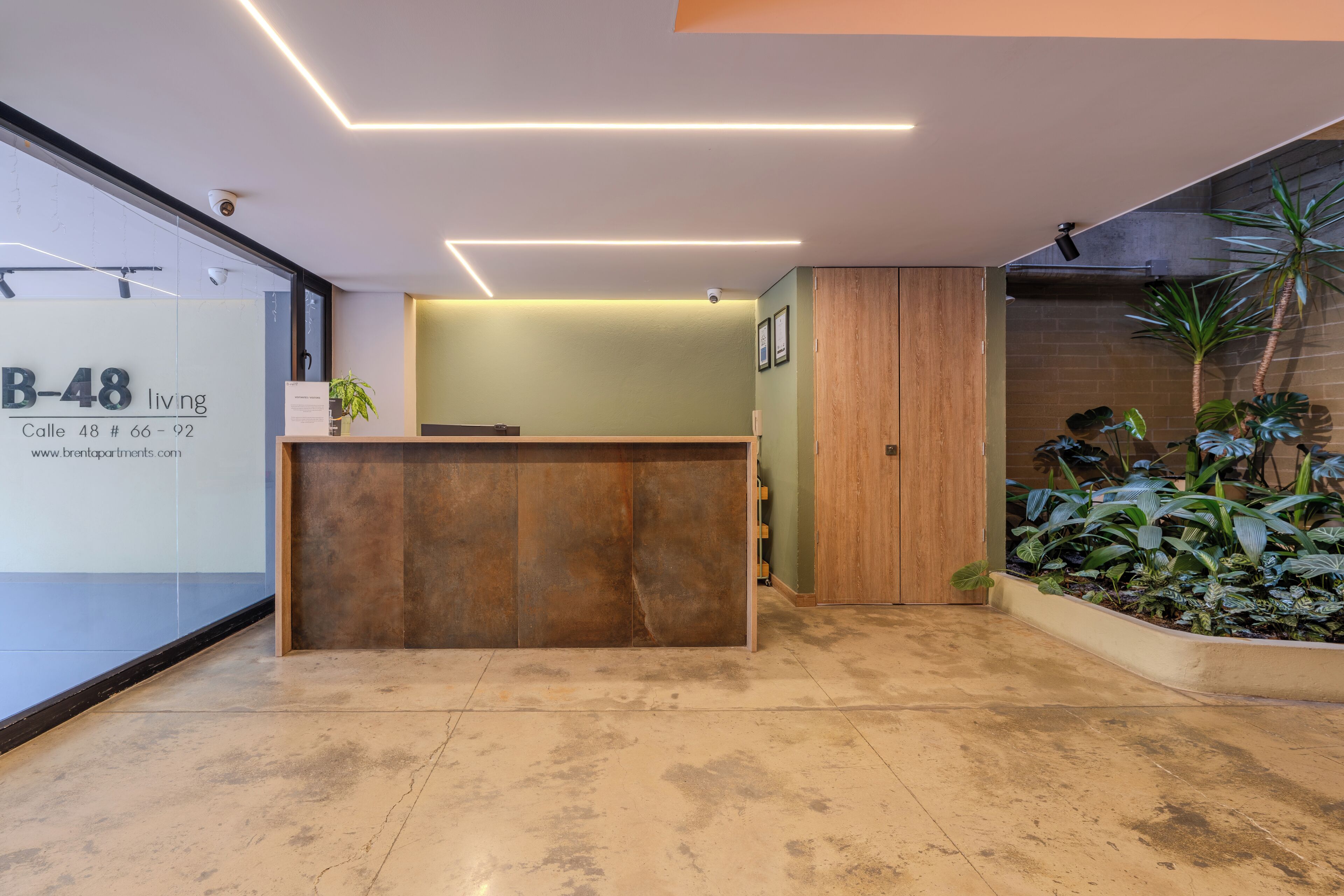 Un espace d’accueil avec un comptoir de réception en bois, un mur végétal et une plante en pot.