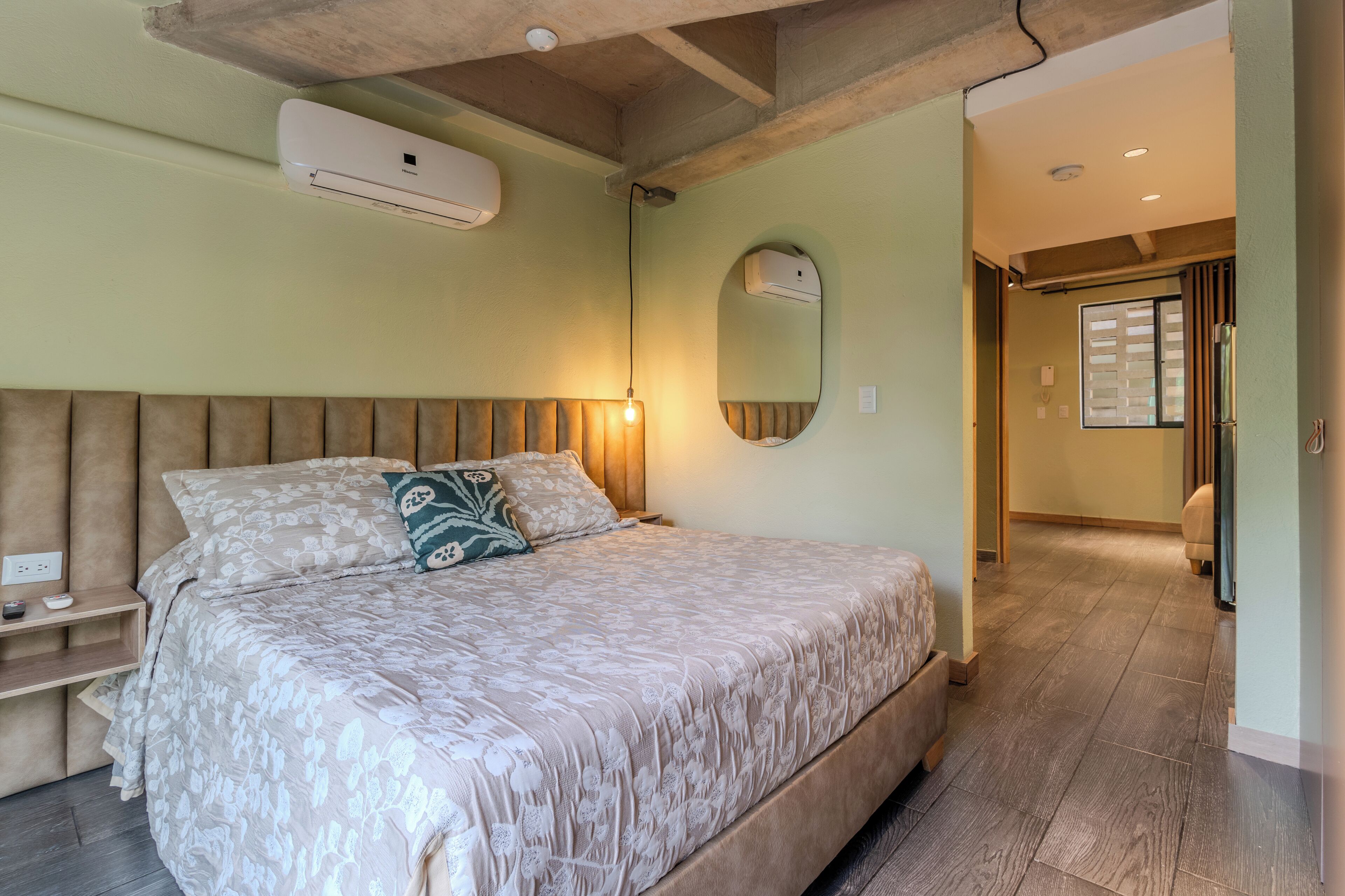 Un dormitorio con cama, mesitas de noche, un espejo y un aire acondicionado.