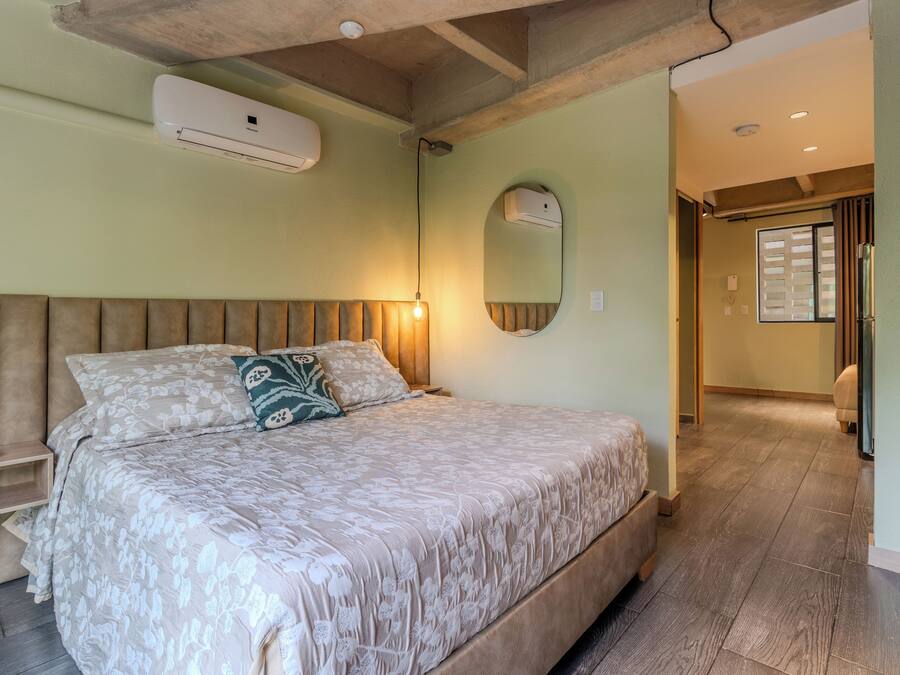 Un dormitorio con cama, mesitas de noche, un espejo y un aire acondicionado.