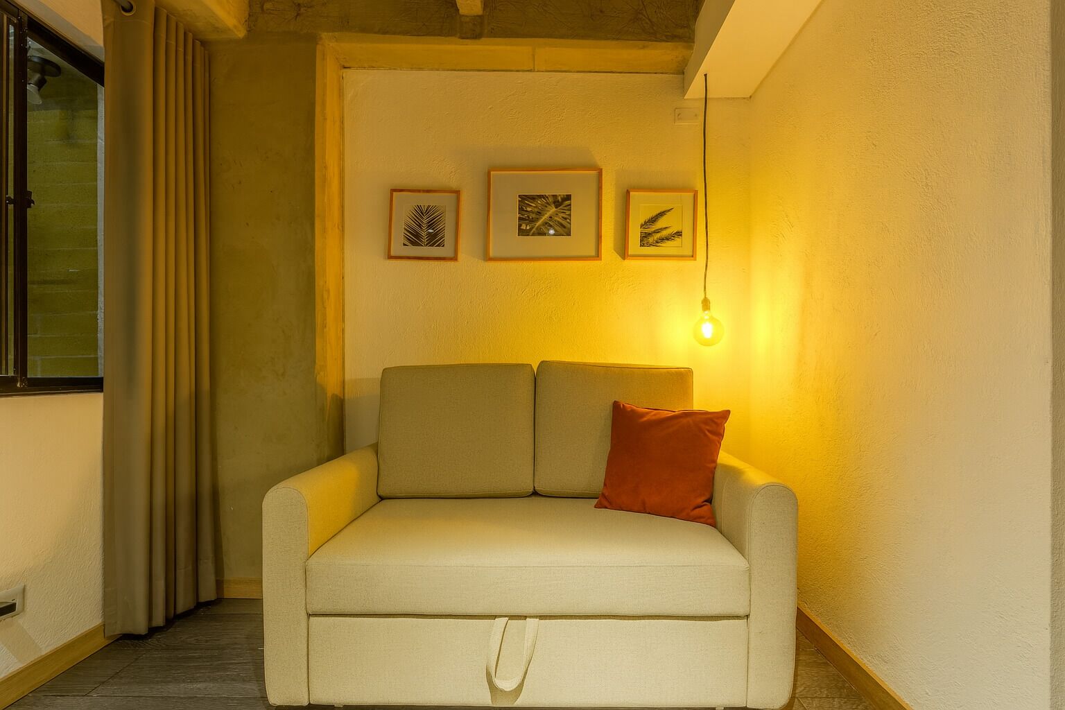 A cozy living room with a sofa, a red pillow, and three framed pictures on the wall.