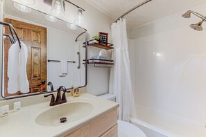 Un baño con lavamanos, espejo, ducha y un estante con artículos de aseo.
