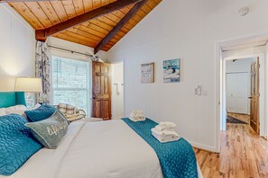 Un dormitorio con techo de madera, una cama con ropa de cama azul y blanca, una silla y una puerta que da a otra habitación.