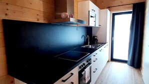 Une cuisine moderne avec des poutres en bois, un plan de travail noir, des meubles blancs et une grande fenêtre.