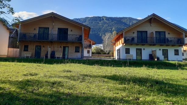 Deux maisons en bois dotées de balcons, un champ verdoyant et une montagne en arrière-plan.