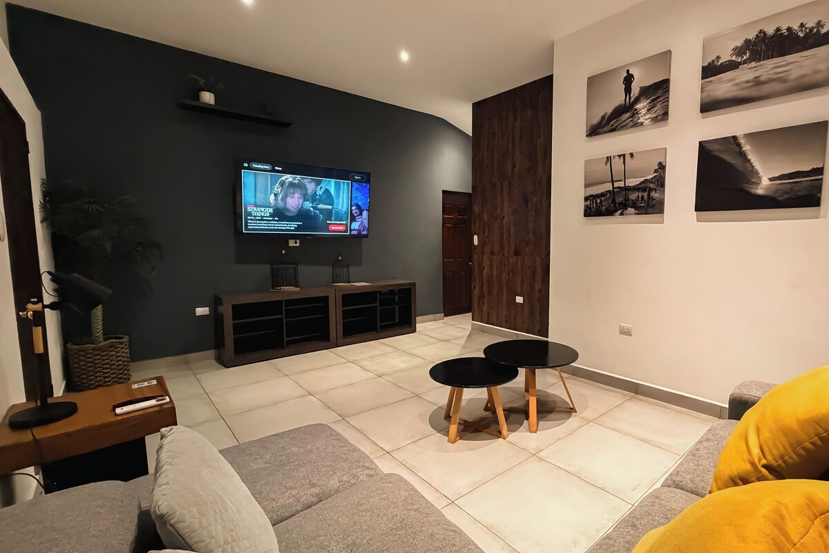Una sala de estar con televisor, dos taburetes negros, un sofá y una mesa de centro.