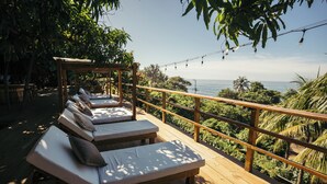 A wooden deck with lounge chairs and a pergola, overlooking a lush landscape and the sea. - El Xalli Hotel (Chiltiupan)