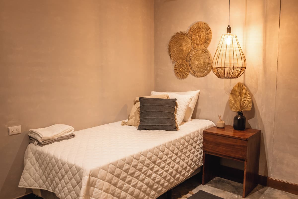 Una cama bien hecha con colcha acolchada, una lámpara de noche y decoración mural.