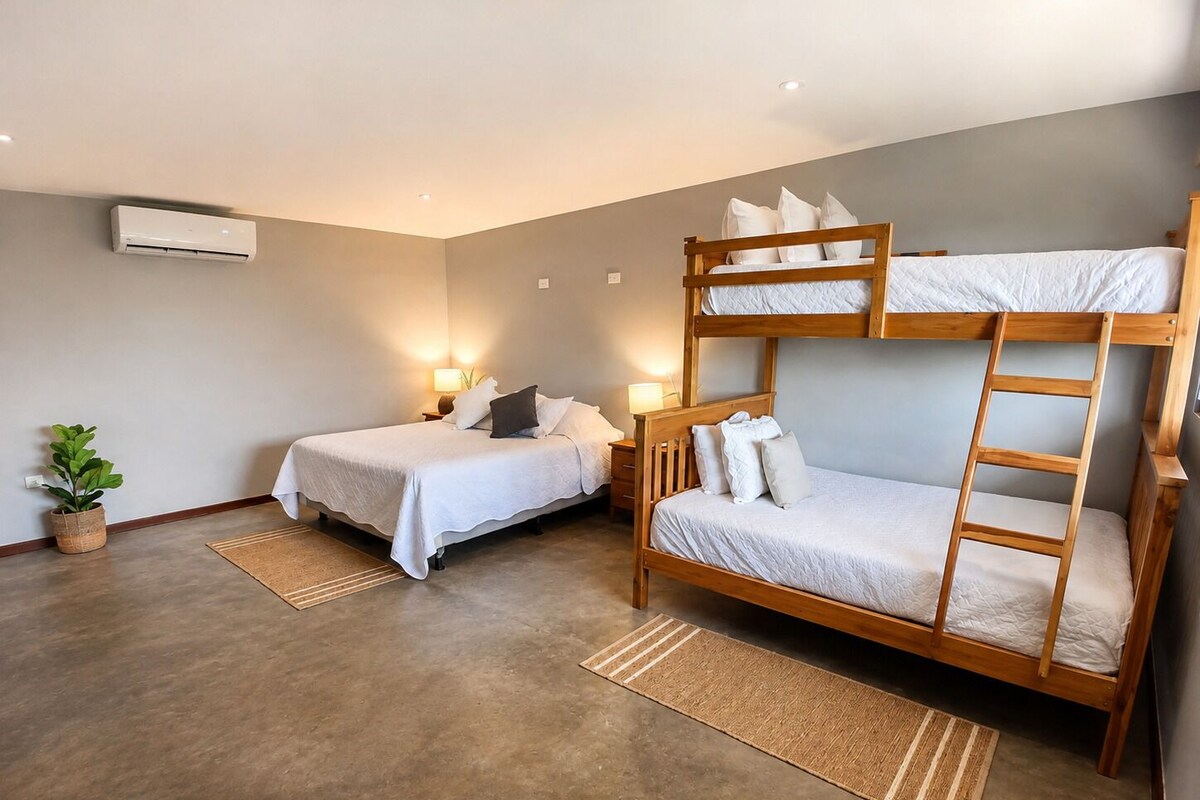 Habitación con dos camas, una litera, una planta en maceta y aire acondicionado de pared.