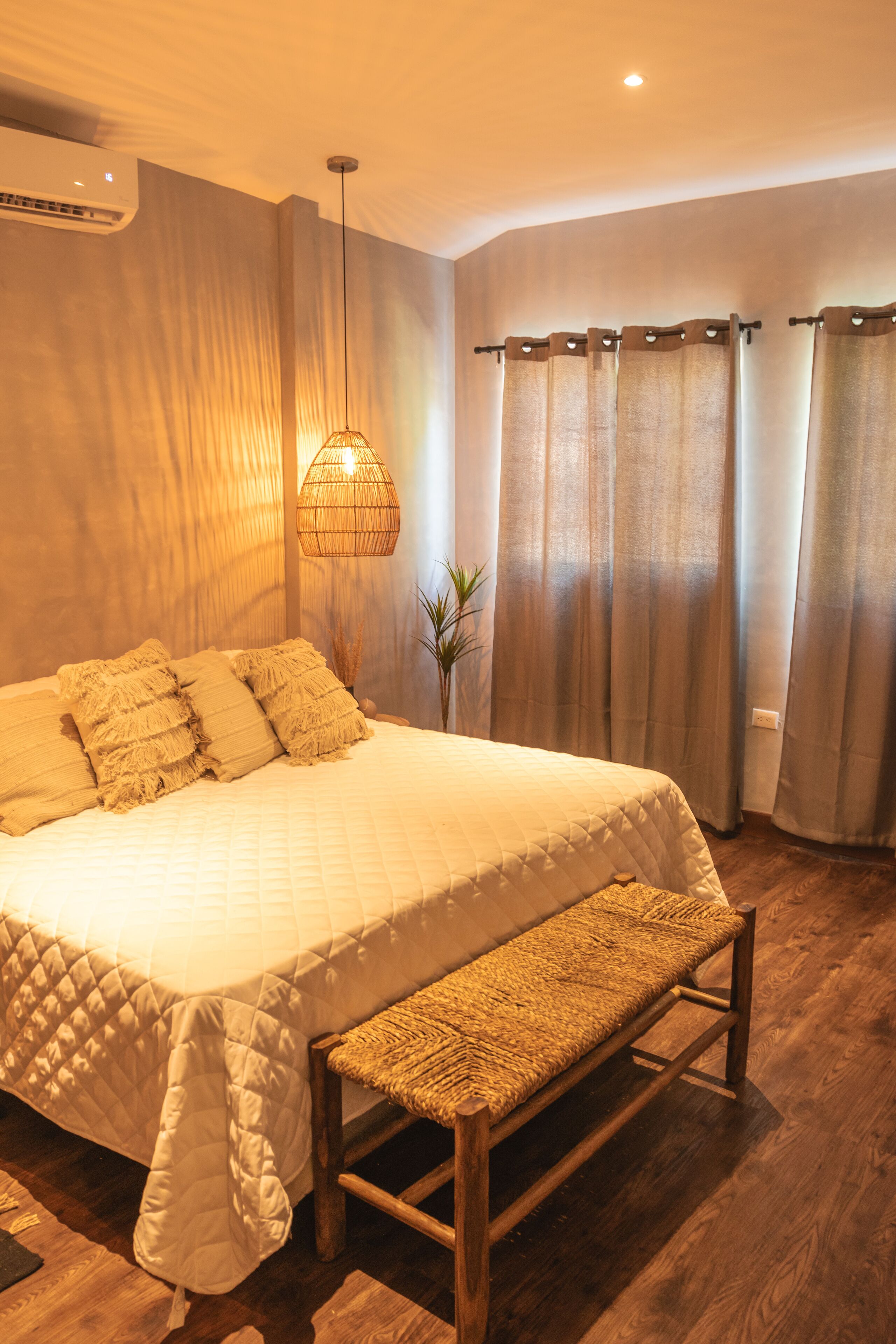 Un dormitorio con una cama grande, un banco, una lámpara colgante y cortinas.