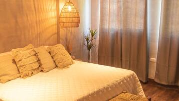 Un dormitorio con una cama grande, un banco, una lámpara colgante y cortinas.
