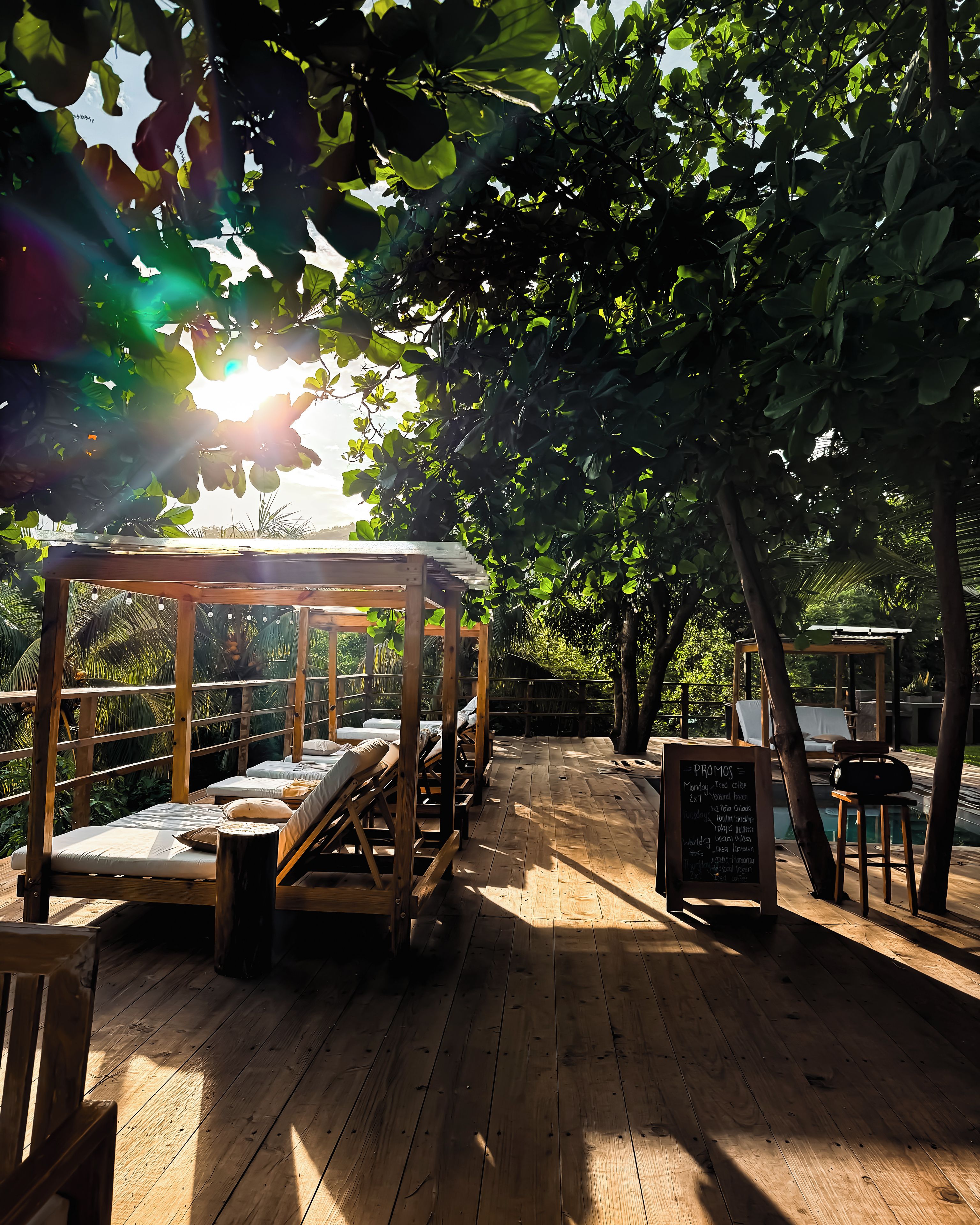 A wooden deck with sun loungers and a wooden pergola, surrounded by lush greenery.