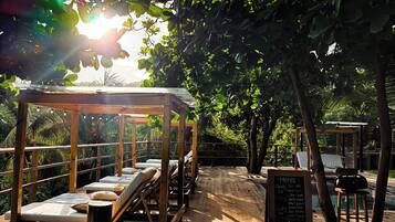 A wooden deck with sun loungers and a wooden pergola, surrounded by lush greenery.