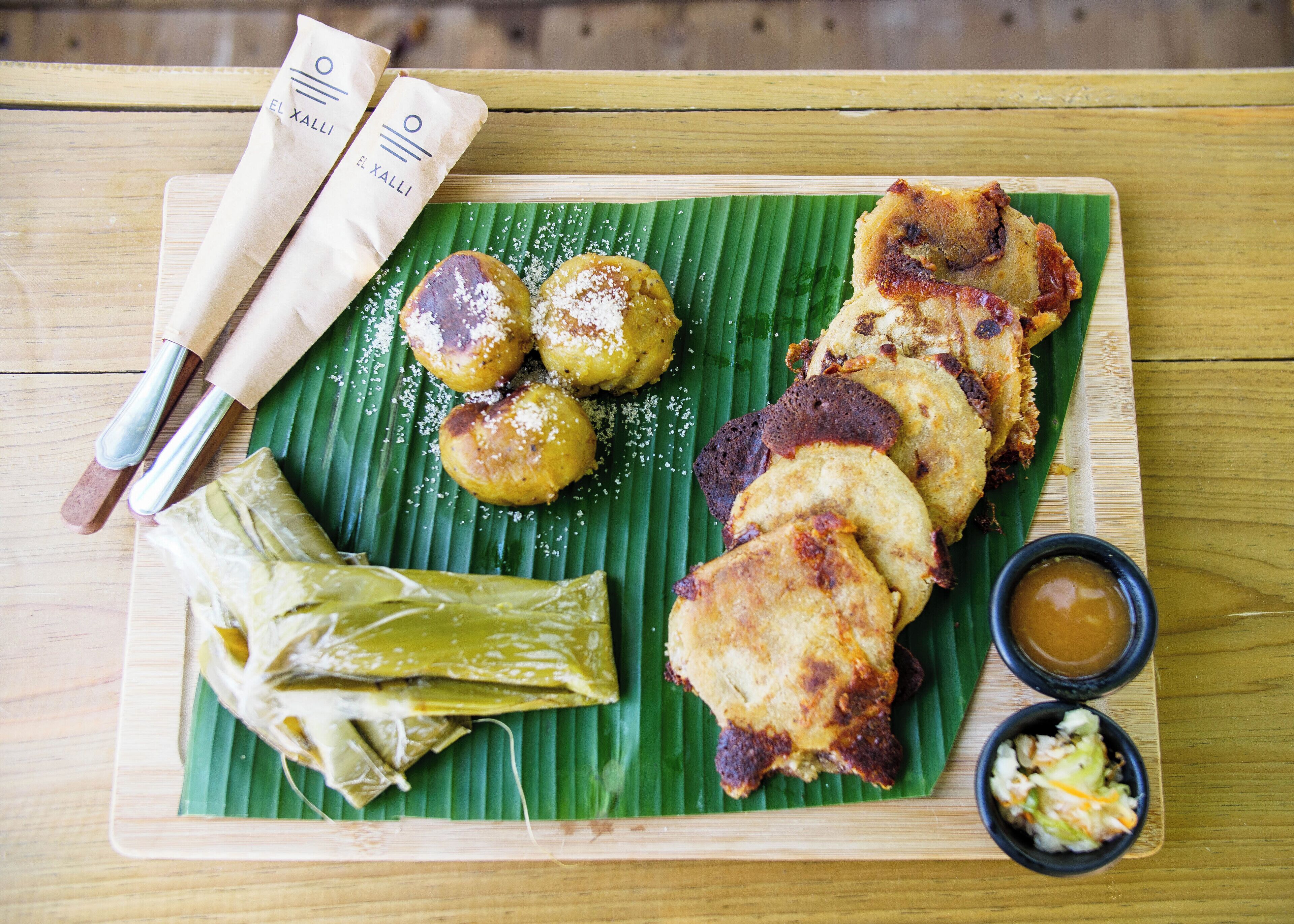 Una mesa de madera con una hoja de plátano sirviendo como plato, incluyendo alimentos fritos y un pequeño recipiente con salsa.
