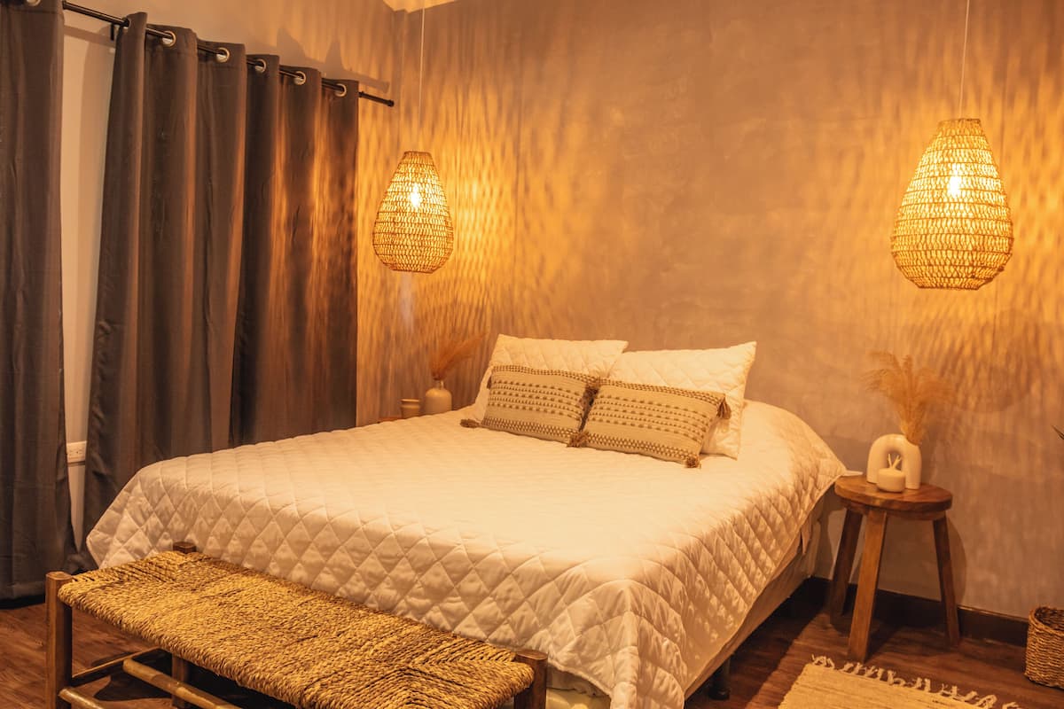A bedroom with a large bed, two bedside lamps, a bench, and a small table with a vase.