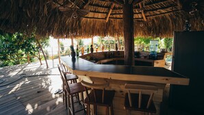 An outdoor bar area with a thatched roof, wooden bar counter, and several stools. - El Xalli Hotel (Chiltiupan)