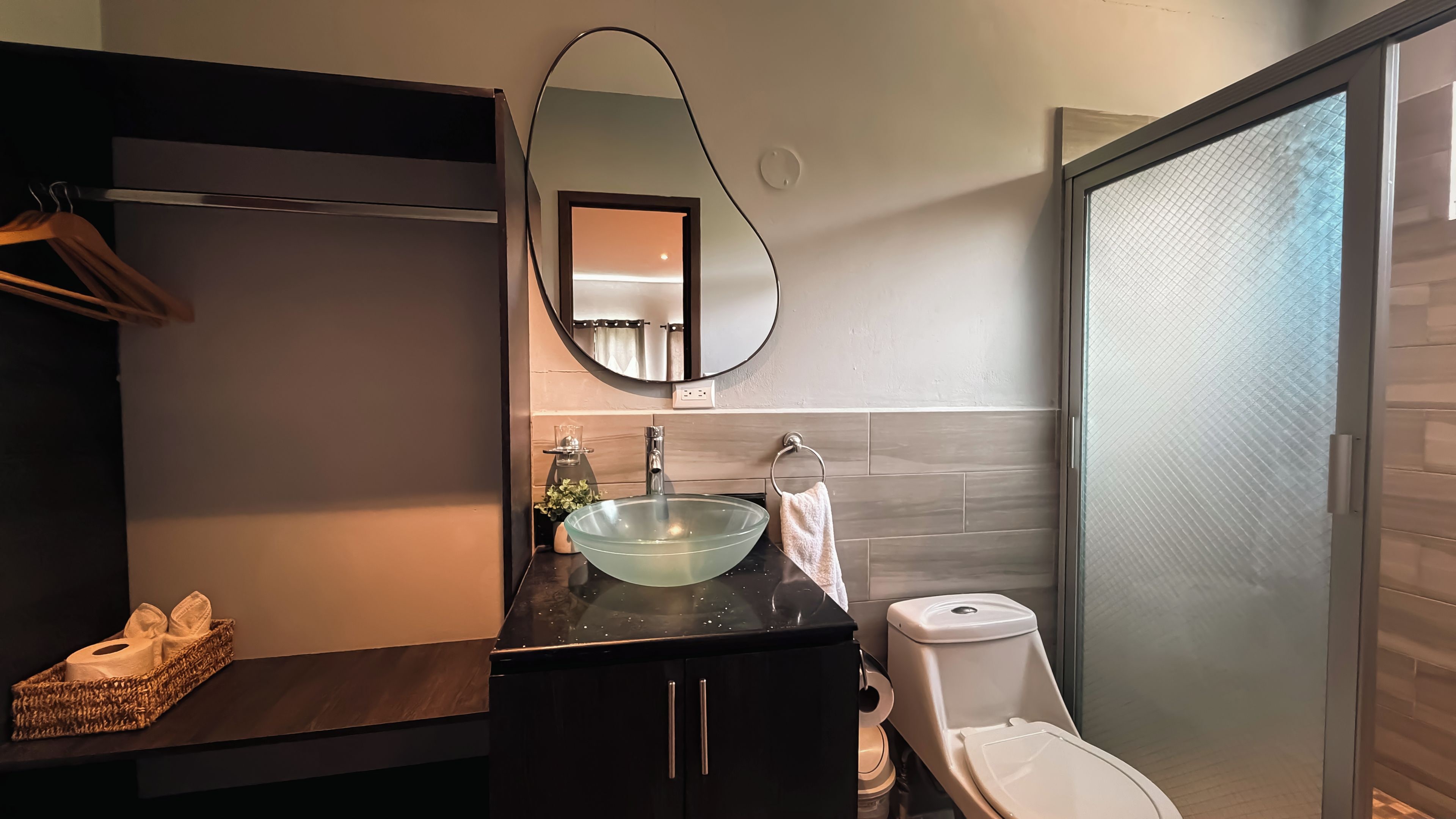 A modern bathroom with a glass sink, dark cabinetry, a towel rack, and a toilet.