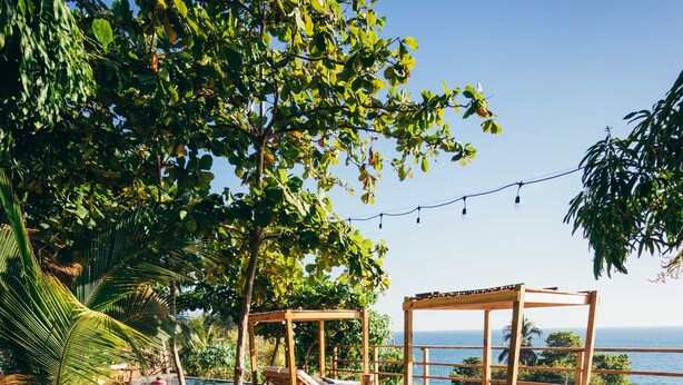 A wooden deck with a swimming pool, lounge chairs, and a view of the ocean. - El Xalli Hotel (Chiltiupan)