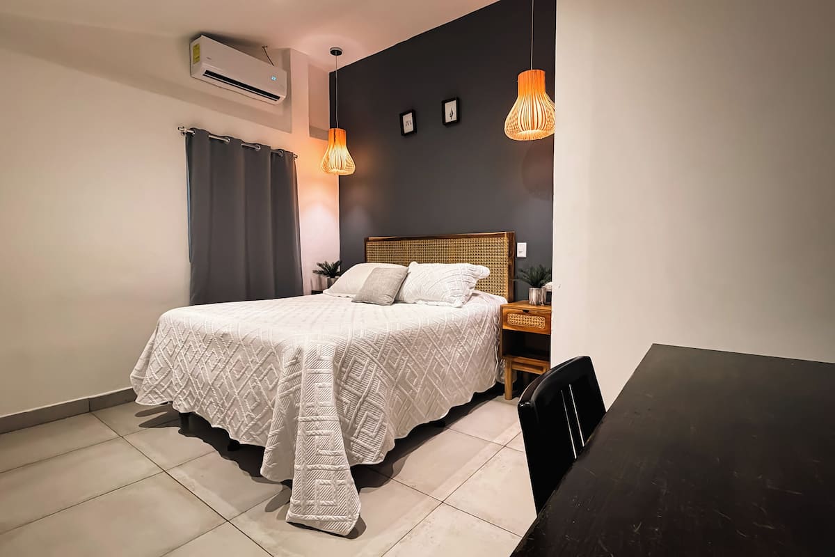 Un dormitorio con cama, mesita de noche, mesa y aire acondicionado.