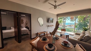 A modern living room with a dining area, a TV mounted on the wall, and a large window offering a view of the outdoors. - El Xalli Hotel (Chiltiupan)