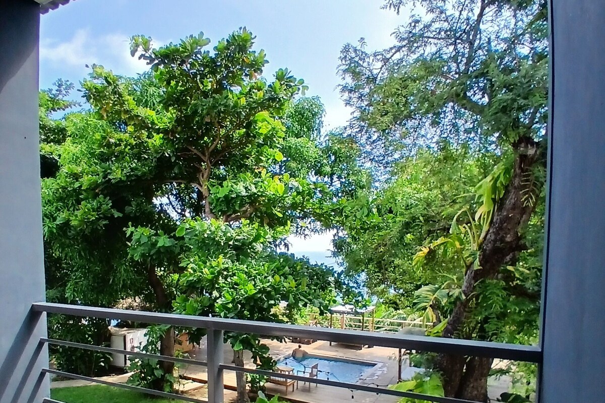 Un balcón con vista a una piscina, vegetación exuberante y cielo despejado.