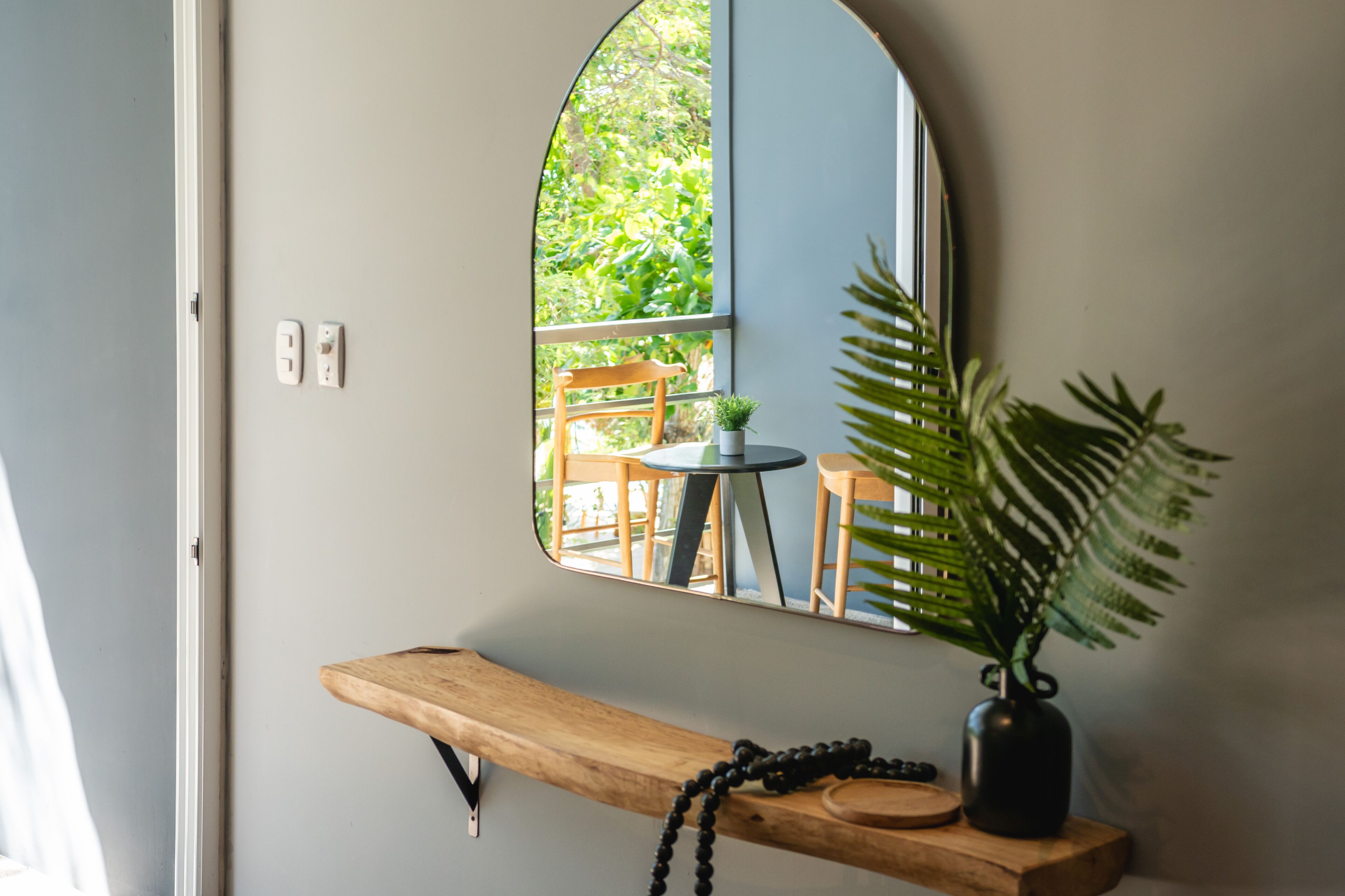 A room with a wooden bench, a mirror, a potted plant, and a small table.