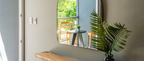 A room with a wooden bench, a mirror, a potted plant, and a small table.