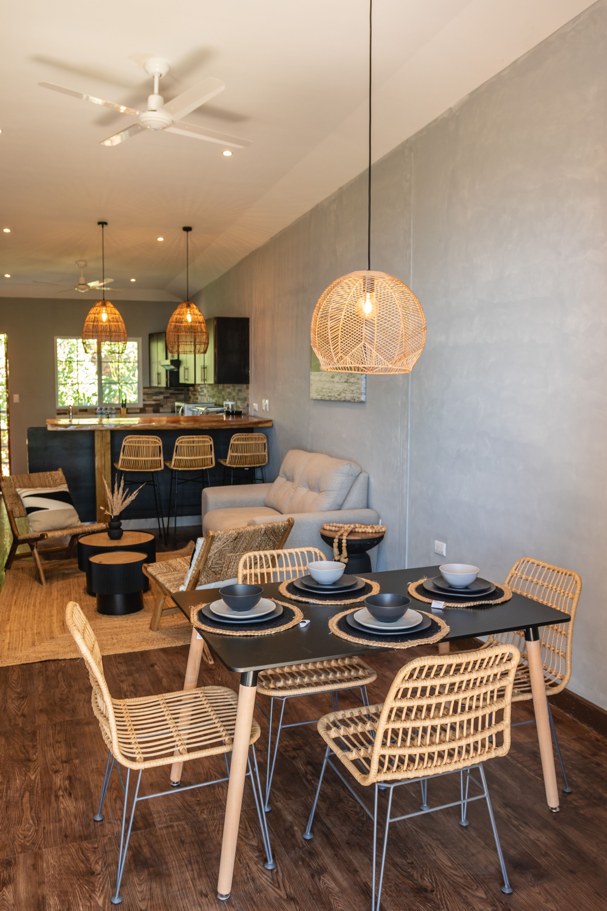A modern dining area with a black table, wicker chairs, and a ceiling fan.
