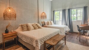 A bedroom with two beds, a wooden bench, a small table, and a window with curtains. - El Xalli Hotel (Chiltiupan)