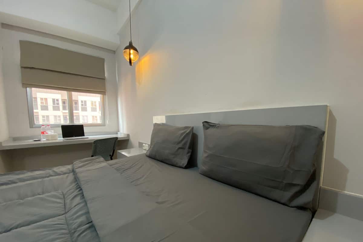 A modern hotel room with a large bed, a desk with a laptop, and a window with a view of buildings.