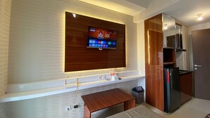 A modern kitchen with a built-in TV, wooden cabinetry, and a small dining area. - Shero Transpark Bekasi (Bekasi)