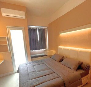 A bedroom with a bed, bedside table, and an air conditioning unit. - Shero Transpark Bekasi (Bekasi)