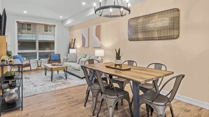 A modern dining area with a wooden table and chairs, a chandelier, and a sofa in the background. - Stylishly Renovated Spring Creek Retreat (Canmore)