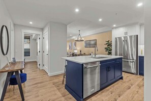 Eine moderne Küche mit Kochinsel, Edelstahlgeräten und einem Essbereich mit Holztisch und blauem Stuhl.