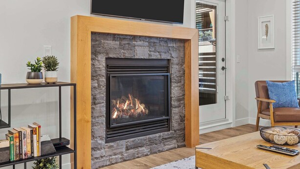 A living room with a stone fireplace, a bookshelf, a coffee table, and a brown leather armchair. - Stylishly Renovated Spring Creek Retreat (Canmore)
