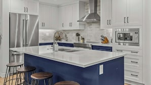A modern kitchen with white cabinets, stainless steel appliances, a central island with stools, and a blue accent wall. - Stylishly Renovated Spring Creek Retreat (Canmore)