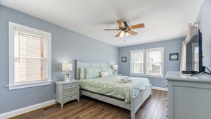 Een slaapkamer met een bed, nachtkastjes, een plafondventilator en een dressoir.