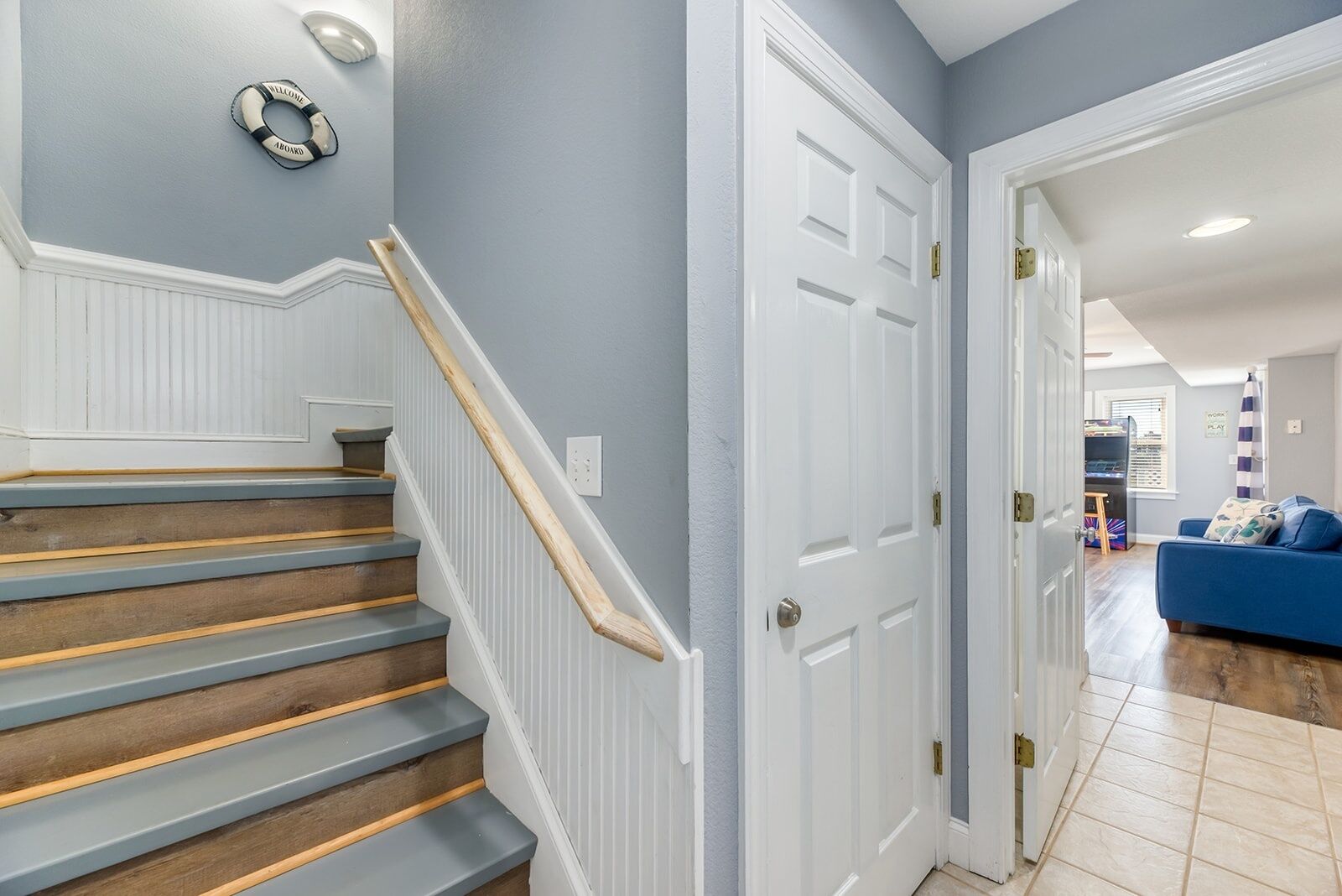 A staircase with wooden steps and a white handrail, leading to a room with a blue couch and a bookshelf.