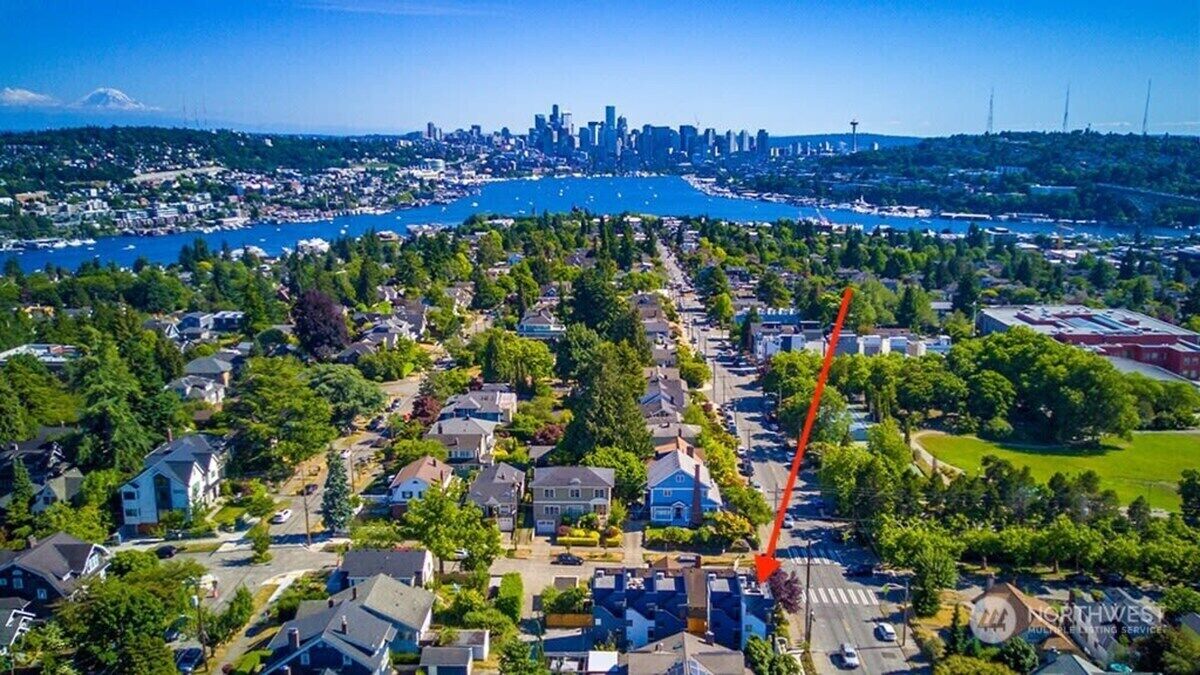 An aerial view of a residential area with houses, a river, and a distant city skyline.