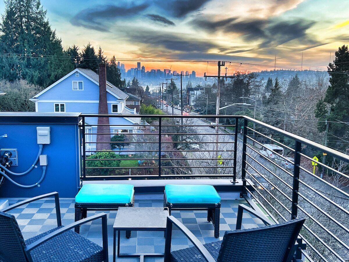 A rooftop terrace with a view of a city skyline, a blue building, and a railing.