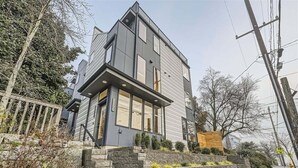 Ein modernes, zweistöckiges Haus mit einer Steintreppe, die zum Eingang führt, umgeben von einer Steinmauer und kleinen Pflanzen.