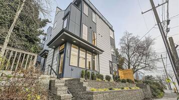 A modern two-story house with a stone staircase leading to the entrance, surrounded by a stone wall and small plants.