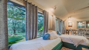 Ein Schlafzimmer mit zwei Betten, großen Fenstern und Blick auf Bäume.