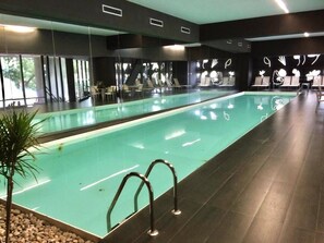 A swimming pool with clear water, surrounded by dark flooring, and a seating area with chairs and tables.