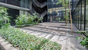 A modern building with a central courtyard, surrounded by glass walls, featuring a staircase, railings, and various plants. - Moderno Departamento En Reforma 284 (Mexico City)