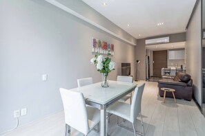 A modern living room with a dining area, a sofa, and a kitchen in the background.