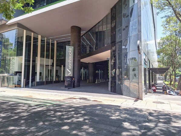 A modern building with a glass facade, a prominent entrance with a vertical sign, and a covered walkway.