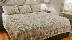 Un dormitorio con una cama grande, una mesita de noche, una lámpara, una ventana con cortinas y suelo de madera.